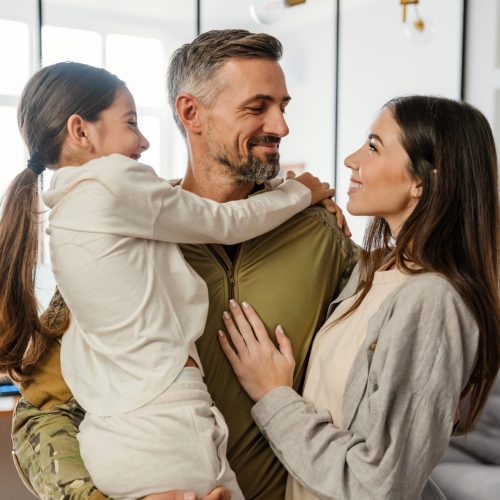 Happy masculine military man smiling and hugging his family indoors